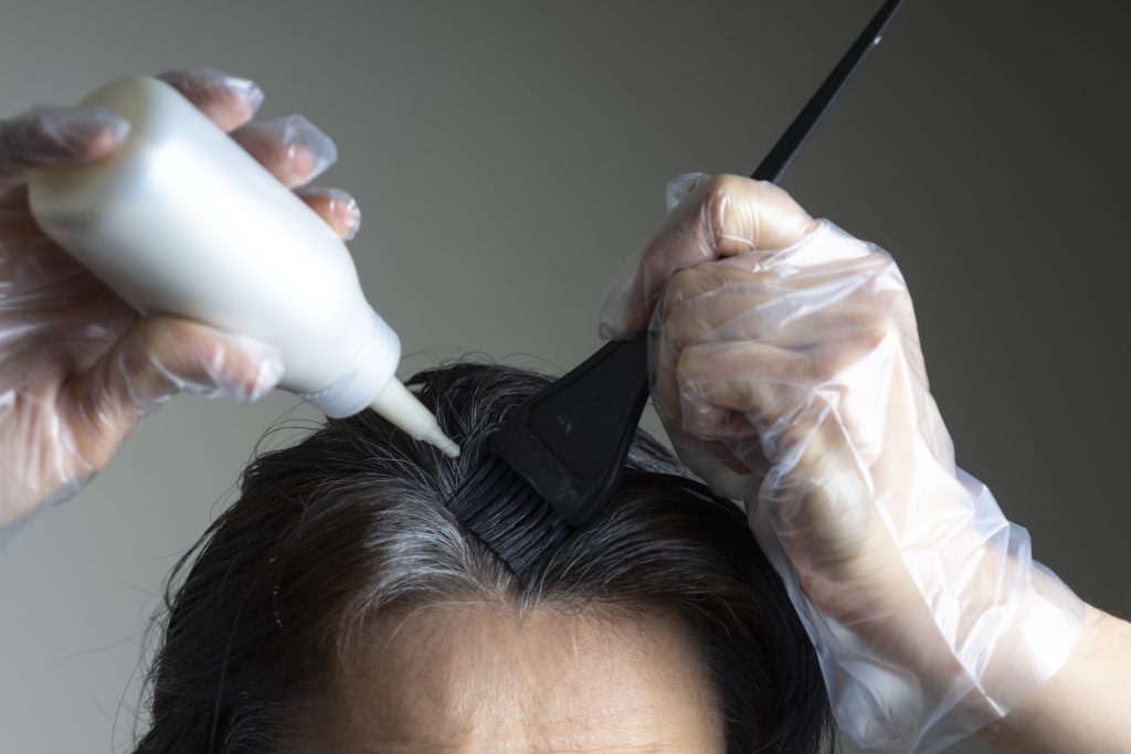 Closeup woman hands dyeing hair using black brush. Middle age woman colouring dark hair with gray roots at home